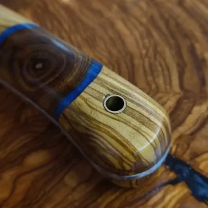 Pieza de monte de 8 cm forjada en Taramundi con empuñadura de olivo estabilizado y un tronquito de falsa acacia rodeado de resina epoxy azul. A falta de la funda en cuero a medida, así queda este precioso cuchillito para ayudarnos en el campo. Perfecto para trabajos rápidos, setas, y cortés puntuales que os surjan. Cómodo de portar en tu mochila, seguro que hará un magnífico trabajo a su dueño.