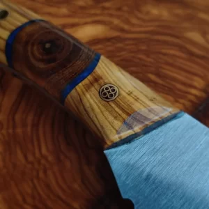 Pieza de monte de 8 cm forjada en Taramundi con empuñadura de olivo estabilizado y un tronquito de falsa acacia rodeado de resina epoxy azul. A falta de la funda en cuero a medida, así queda este precioso cuchillito para ayudarnos en el campo. Perfecto para trabajos rápidos, setas, y cortés puntuales que os surjan. Cómodo de portar en tu mochila, seguro que hará un magnífico trabajo a su dueño.